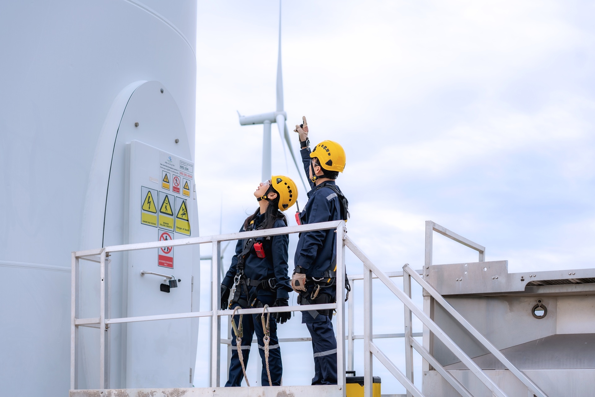 Two people with climbing gear looking up at a windmill